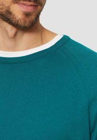 Turkusowy sweter dzianinowy z prążkowanym okrągłym dekoltem i białym akcentem. Charakteryzuje się miękką fakturą i kontrastowym szwem wzdłuż szwów.