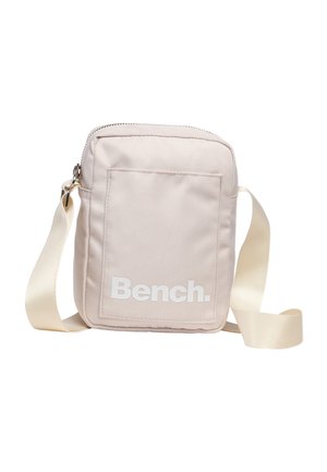 Kleine beige crossbodytas met voorvak en brede verstelbare riem, met wit "Bench." logo op het vak.