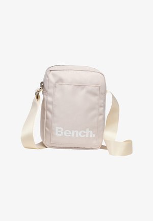 Kleine beige crossbodytas met voorvak en brede verstelbare riem, met wit "Bench." logo op het vak.