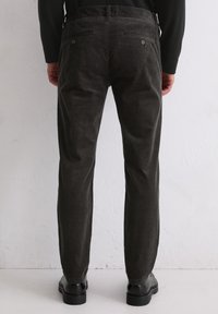 Un pantalon en velours côtelé gris foncé présente une coupe droite, une texture subtile et deux poches arrière avec des fermetures à bouton. La paire est présentée avec des chaussures noires.