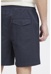 Marineblauwe herenshorts met een elastische tailleband, voorzien van een knoopsluiting op het achterzakje en een gladde, gestructureerde stof.