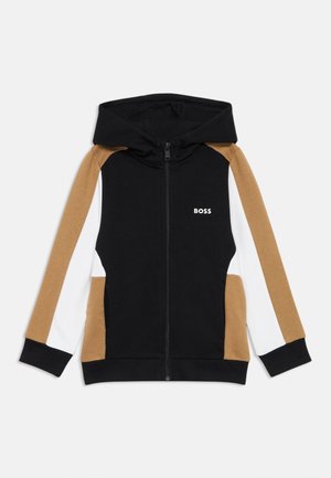 Sweat à capuche avec une fermeture zippée à l'avant. Les couleurs principales sont le noir, le marron et le blanc, avec des panneaux contrastants et un petit logo.