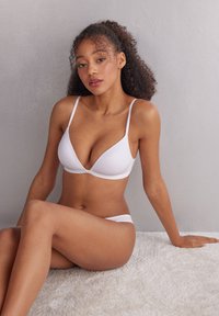 Soutien-gorge blanc avec décolleté plongeant et fines bretelles, assorti de culottes correspondantes. Texture lisse, design minimaliste et sans matériel visible.