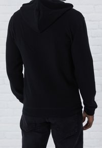 Sudadera con capucha negra, de textura suave, de mangas largas y corte holgado. La parte posterior presenta una costura centrada y un dobladillo acanalado.