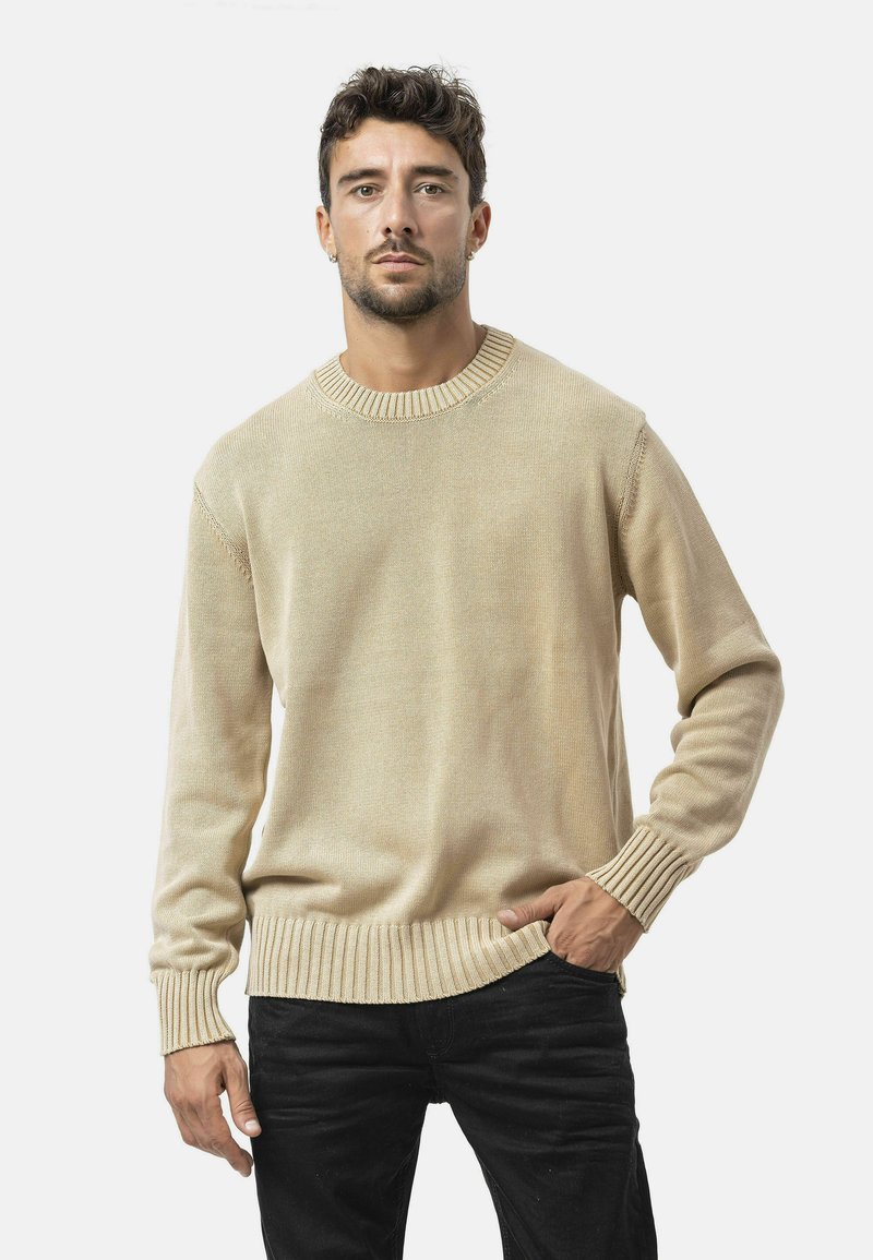 Helles beiges, geripptes Sweatshirt mit rundem Hals, langen Ärmeln und strukturiertem Stoff; getragen mit lockeren schwarzen Jeans.