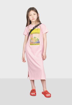 Robe en coton rose avec des manches courtes et un imprimé graphique, associée à des sandales rouges à glisser affichant le mot "AMOUR."