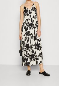 Svart- och vitblommig maxiklänning med tunna axelband, V-ringning och rynkad midja. Tillsammans med svarta mule-skor och en liten svart handväska.