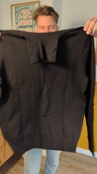 Pullover nero tenuto in posizione verticale, con maniche lunghe, polsini e orlo a coste, superficie liscia, vestibilità standard e scollo rotondo.