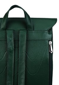 Green leather backpack with a textured surface, featuring a front flap, two straps, and a silver zipper detail on the side.