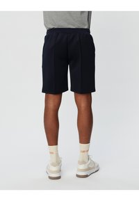 Navy blue athletic shorts with a smooth texture, featuring a comfortable elastic waistband and two side pockets. Worn with cream socks and sneakers.