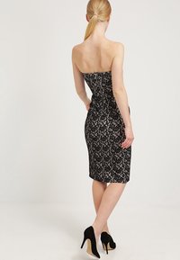 Axellös svart spetsklänning med en åtsittande silhuett, knälång, med dragkedjestängning i ryggen och en slät textur.