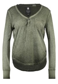 Langärmliges olivgrünes Hemd mit V-Ausschnitt, verblasstem Muster, Brusttasche und abgerundetem Saum. Hergestellt aus weichem Baumwollmaterial.