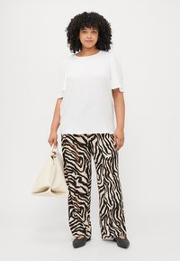 White short-sleeve top paired with beige and black zebra-print wide-leg pants, holding a cream-colored bag. Smooth textile, relaxed fit.