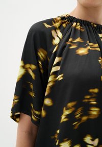 Blusa nera con scollatura arricciata, maniche corte e tessuto fluido, caratterizzata da un motivo astratto in oro e giallo su tutta la superficie.
