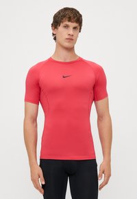 Rdeča športna majica s kratkimi rokavi, izdelana iz raztegljivega materiala, z črnim logotipom Nike na sprednji strani. Prilagojena zasnova in gladka tekstura.