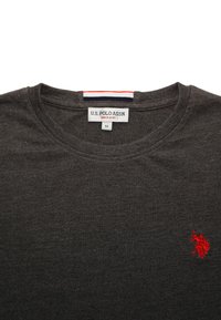 Tmavohnedé tričko s okrúhlym výstrihom, na ktorom je vyšívané červené logo polohráča na hrudi a štítok U.S. Polo Assn. na výstrihu, veľkosť stredná.