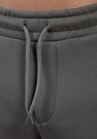 Grå sweatpants med elastisk talje og flettede snore, med sidelomme og glat tekstur.