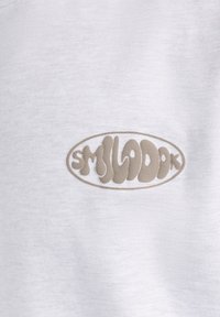 Sudadera de algodón blanca con un logo ovalado texturizado en beige que presenta la palabra "SMILADOK" en una fuente juguetona y ondulante en el centro.