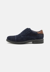 Scarpa in suede blu navy con accentatura in pelle marrone sul tallone e cuciture a contrasto. Suola piatta in gomma con finitura texturizzata.