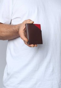 Portafoglio in pelle marrone con uno scomparto rosso per le schede e bordi cuciti, tenuto in mano, caratterizzato da un design compatto e rettangolare.
