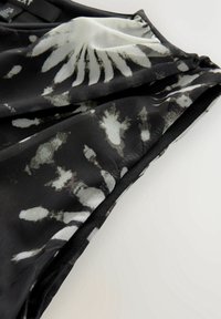 Tessuto a motivi bianco e nero con una superficie morbida, drappeggiato con un bordo liscio e design floreali astratti che creano contrasto.