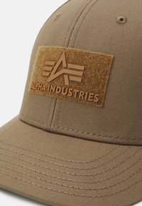 Brun Alpha Industries kasket med syede sømme og en velcro-lap med brandlogo og navn foran.