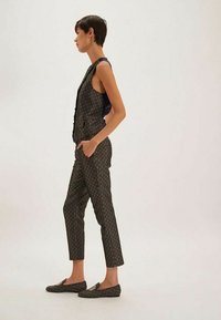 Ensemble de gilet et pantalon noir à motifs, présentant des motifs géométriques complexes. Accompagné de chaussures à enfiler assorties avec un détail de logo.