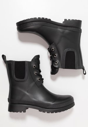 Bottes de pluie noires jusqu'à la cheville avec semelles texturées, lacets à l'avant et panneaux élastiques sur les côtés, présentées sur un fond blanc.