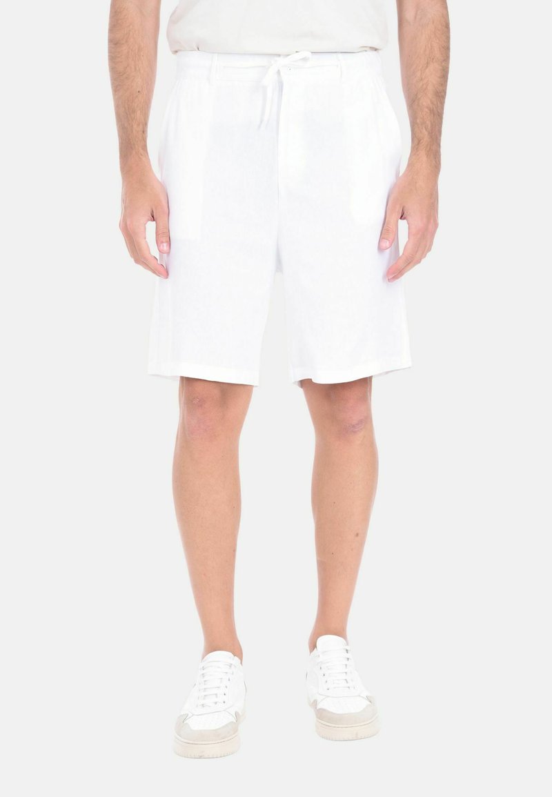 Shorts bianchi in lino con vita elastica e cordoncino, caratterizzati da un fit rilassato e una lunghezza fino al ginocchio. Indossati con sneakers bianche.