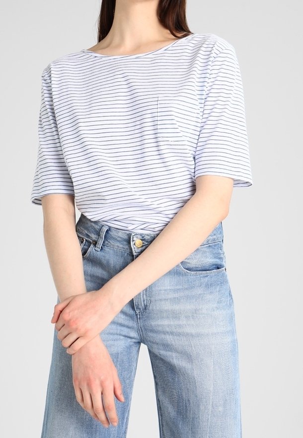 T-shirt blanc avec des rayures horizontales navy, à manches courtes et une poche. Assorti à un jean taille haute bleu clair. Style décontracté.