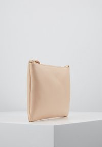 Pudrově růžový kožený sáček s texturovaným povrchem, zipové uzavření na vrchu a minimalistický design. Žádné viditelné kování ani akcenty.