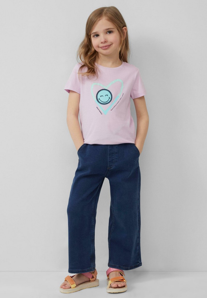 Roze katoenen T-shirt met een grafisch ontwerp van een lachend gezicht en een hart, gecombineerd met donkerblauwe wijdvallende jeans en tan sandalen.