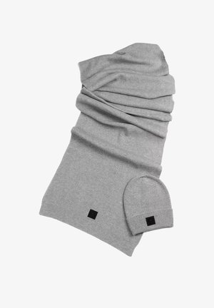 Écharpe en tricot côtelé gris avec bonnet assorti ; présente une finition texturée et un petit logo noir sur les deux articles.