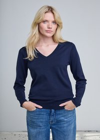 Pull marine à manches longues avec col en V, fabriqué dans un matériau côtelé lisse, associé à un jean bleu clair. Le modèle pose les mains dans les poches.