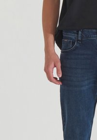 Jeans de denim azul oscuro con corte ajustado, que presentan bolsillos frontales, bragueta con cremallera y detalles de costura sutil a lo largo de las costuras.