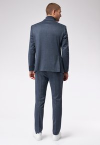 Completo blu navy su misura con blazer strutturato con rever a punta e pantaloni slim fit coordinati. Sneakers bianche completano il look.