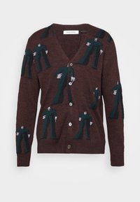 Brun kofta med ett mönster av gröna figurer med vita händer, V-halsdesign, sex knappar och ribbade ärmslut. Mjuk textur.