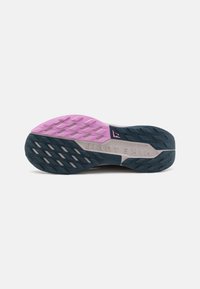 Suela de zapatilla de trail de Nike con una base de goma azul y rosa, con patrones de relieve texturizados, acentos grises y detalle en relieve "NIKE TRAIL".
