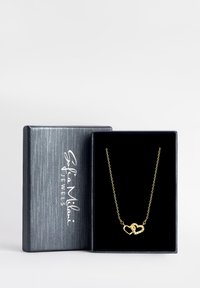 Collana d'oro con design a cuore intrecciato, caratterizzata da piccole pietre trasparenti; presentata in una scatola per gioielli nera con texture.