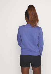 Lila sweatshirt med rund halsringning, ribbstickade muddar och fåll, i kombination med svarta shorts. Tyget verkar mjukt och avslappnat.