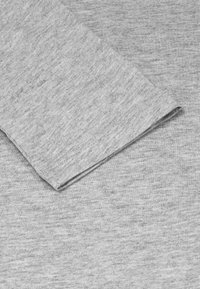Grau Baumwollstoff mit weicher Textur, der einen gefalteten Ärmel und Saum aufweist. Das Material ist leicht meliert und zeigt subtile Farbvariationen.
