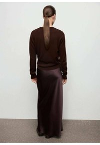 Suéter marrón de manga larga, combinado con una falda maxi de satén marrón oscuro. Textura suave, silueta ajustada y detalle de abertura lateral visible.