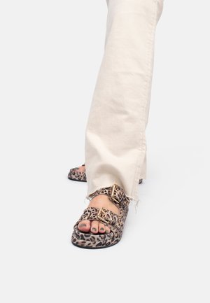 Sandali con stampa leopardata, dotati di due fibbie regolabili, suole piatte e una finitura testurizzata, abbinati a pantaloni color crema con orlo sfrangiato.