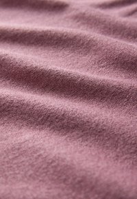 Primo piano di un morbido tessuto testurizzato in mauve tenue, con delicate pieghe e un fine motivo a maglia.