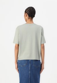 Light green cotton T-shirt with short sleeves, round neck, and a cropped fit, paired with a high-waisted, blue denim skirt.
