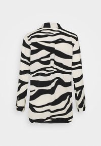Chemise à manches longues en tissu léger, présentant un motif zèbre noir et blanc. Design à col avec une ouverture arrière et des manches à revers.