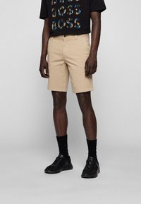 Beiga shorts i bomull med en klassisk design, platt front, sidofickor och rak passform. Bärs med en svart grafisk t-shirt.