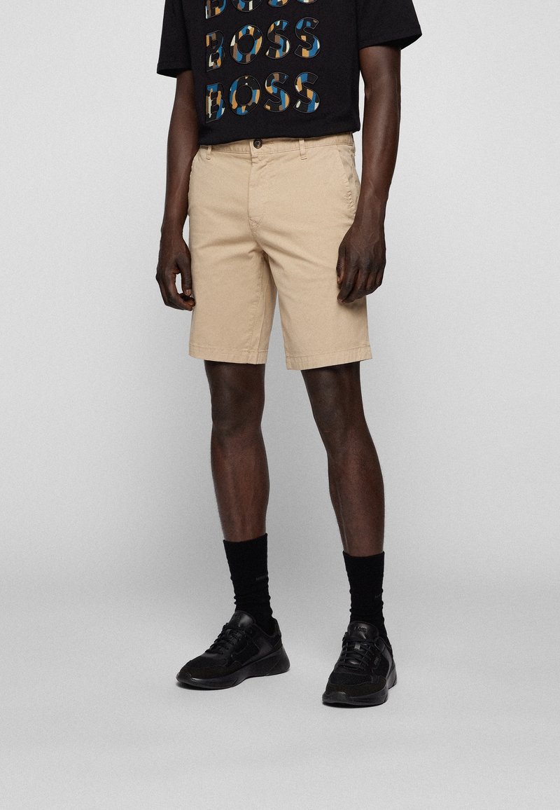 Beiga shorts i bomull med en klassisk design, platt front, sidofickor och rak passform. Bärs med en svart grafisk t-shirt.