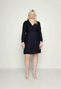 Vestido azul-marinho com decote em V, mangas longas e cintura franzida. Apresenta um padrão texturizado e cai acima do joelho, combinado com sandálias claras.