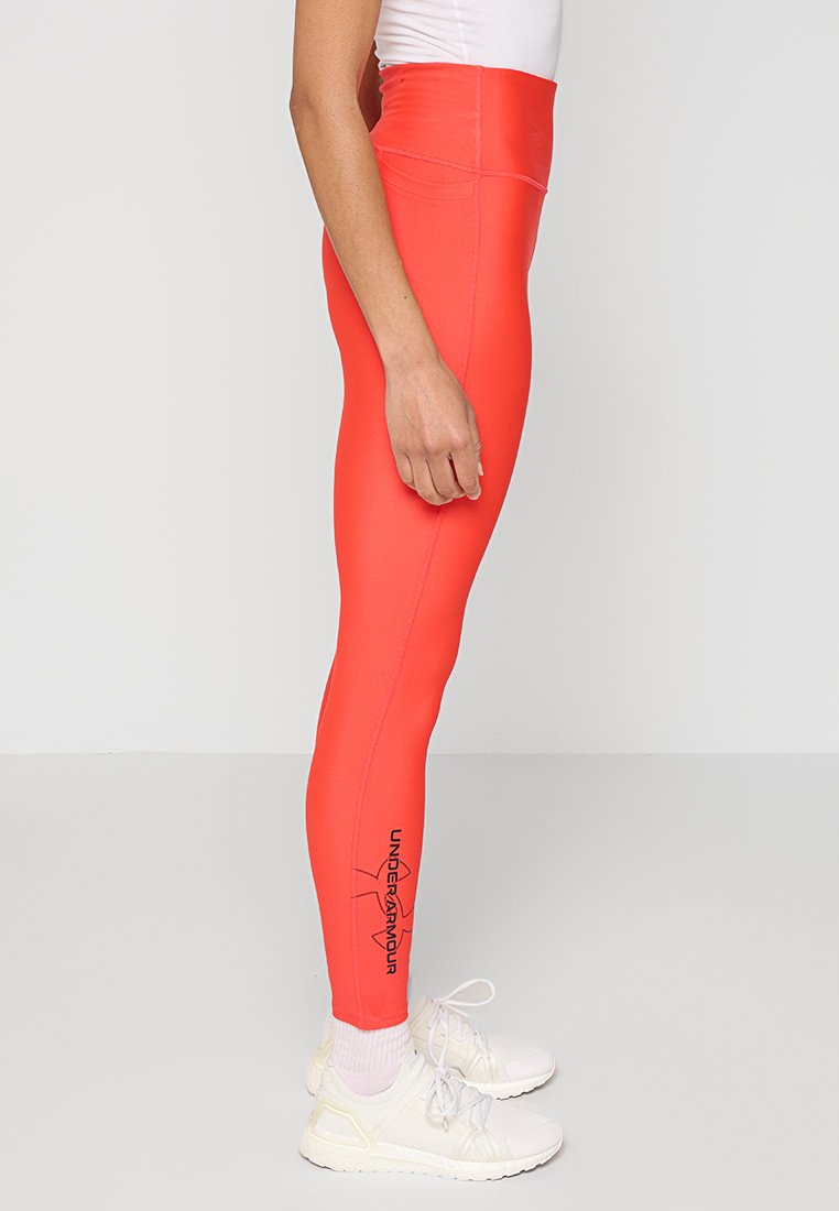 Leggings de tiro alto y ajustados en un vibrante color coral, fabricados con un material elástico, que presentan un logo negro en la parte inferior de la pierna y una textura suave.